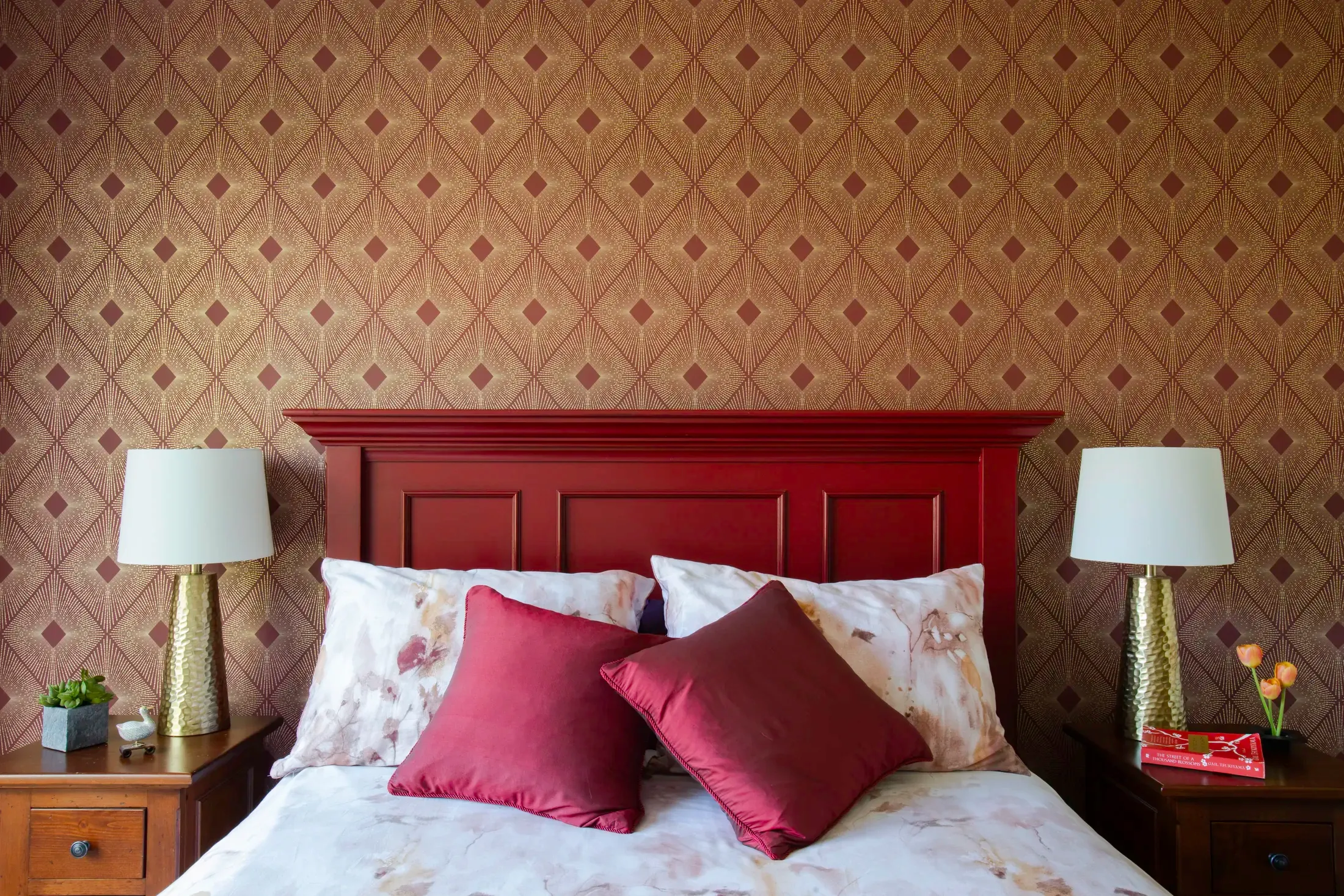 A tailored bedroom with geometric wallcovering and a deep red wood bed